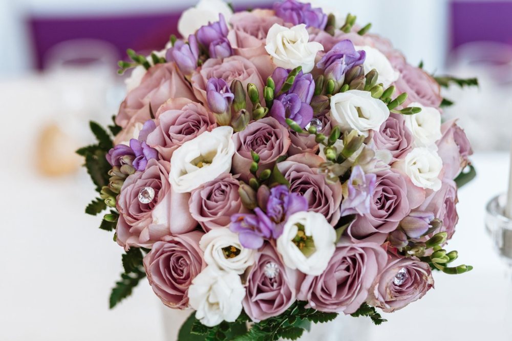 Un ramo de novia con rosas malva empolvado, fresias lilas y flores blancas