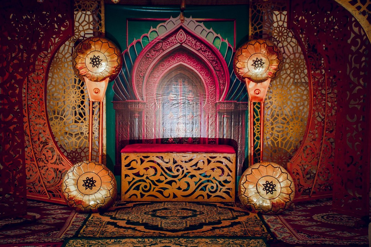 An ornately decorated lounge setup with patterned screens, gold poufs, and warm lighting